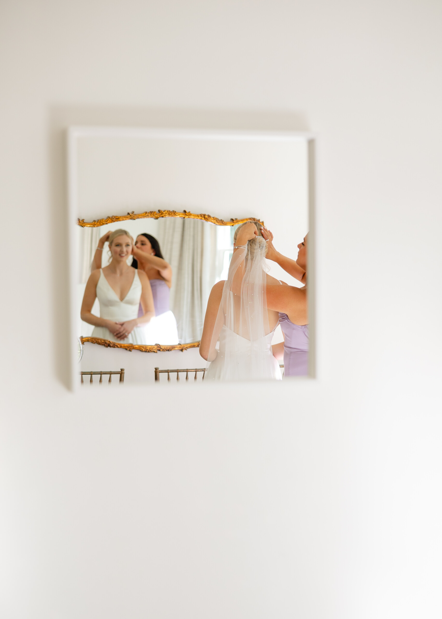 Bride adjusting her veil in a window’s soft natural light before her wedding