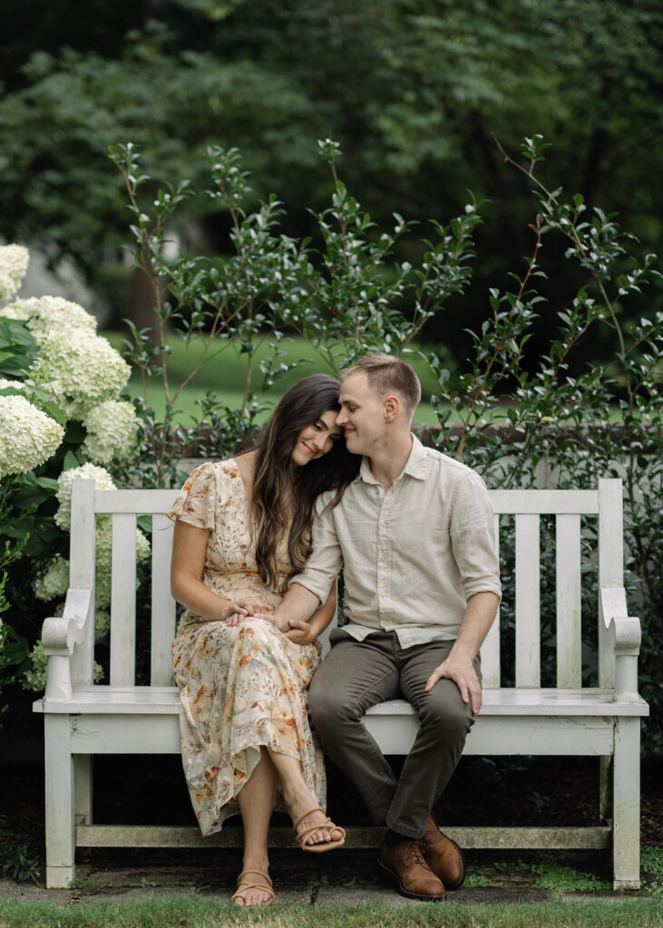 Engaged couple sitting in the hydrangea bushes at Reynolda Gardens in Winston-Salem, NC. North Carolina wedding photographer. Engagement photographer in Winston-Salem NC.