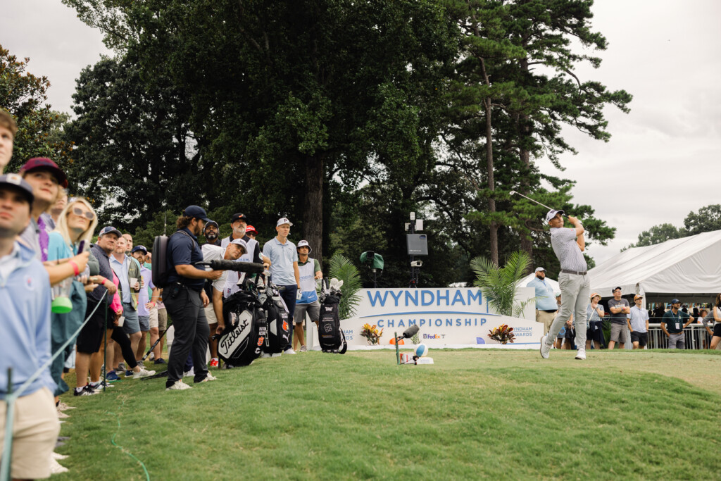 Vibrant crowd watching a golfer tee off at the Wyndham Championship